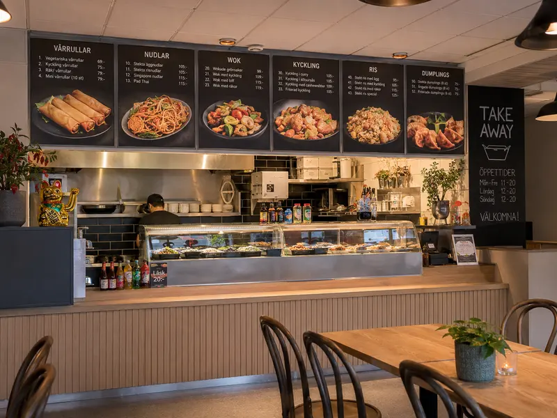 Asiatisk restaurang med menytavlor för nudlar, wok och dumplings ovanför disken