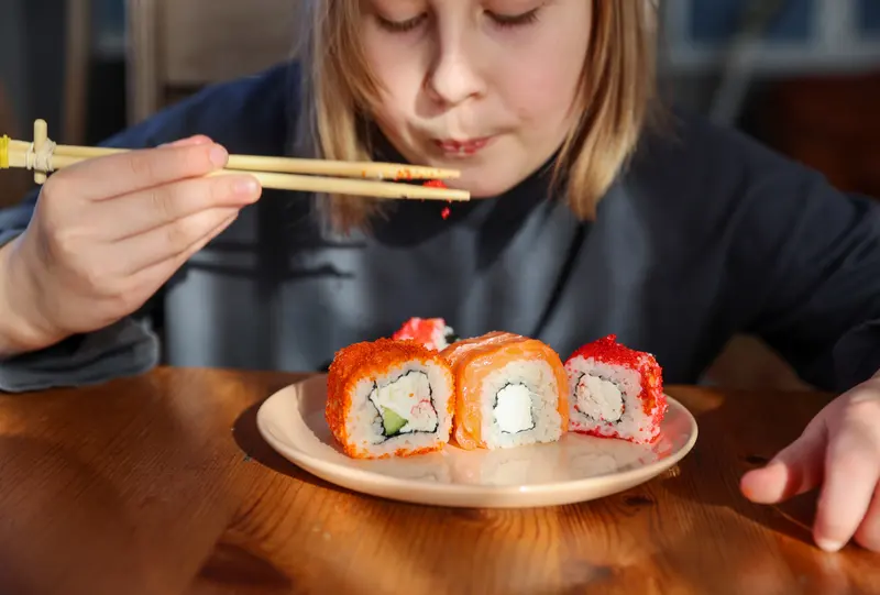 Barn äter sushi med pinnar vid ett bord på en restaurang
