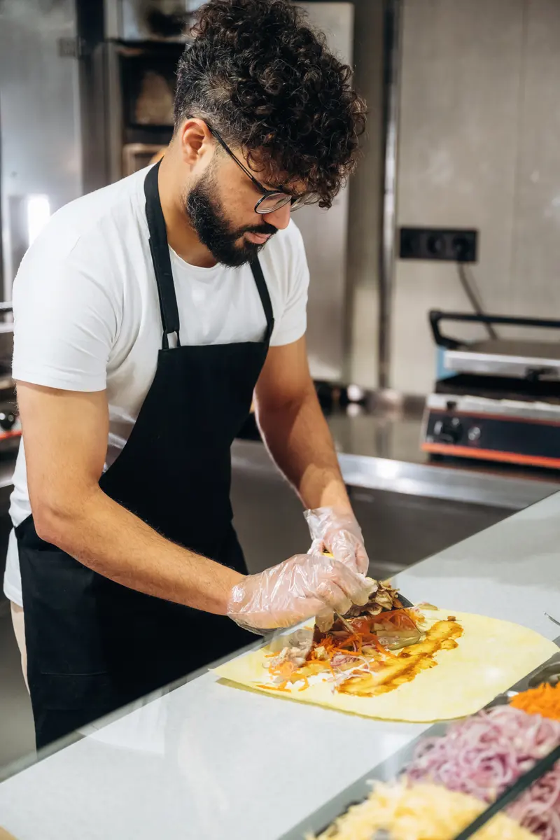 Kock rullar ihop en kebabrulle på skärbrädan i ett storkök