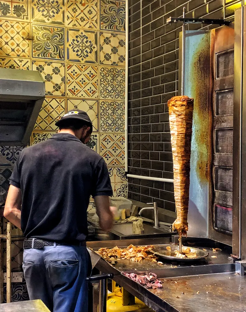Man arbetar vid kebabspettet i en liten grillokal med kaklad vägg