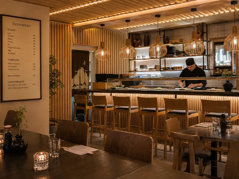 Restaurang med öppet kök, träpanel och barstolar vid disken