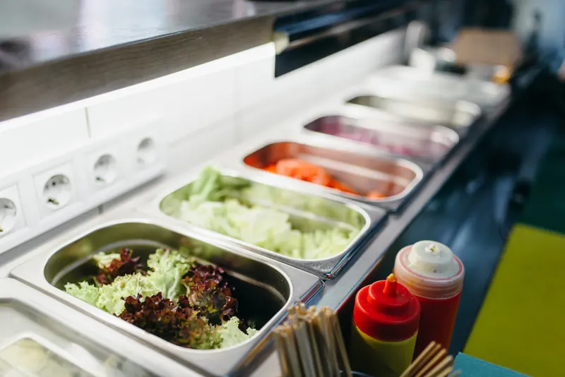 Rostfria kantiner med sallad och grönsaker i en kyld salladsbar