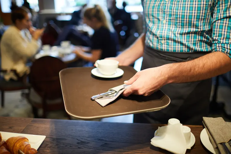 Servitör bär en bricka med kaffe och bakverk genom ett café