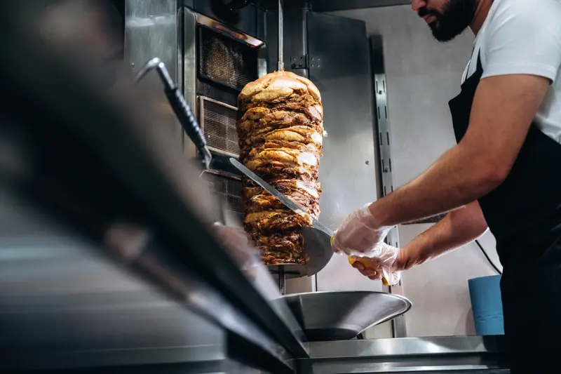 Händer skär tunna skivor kött från ett kebabspett