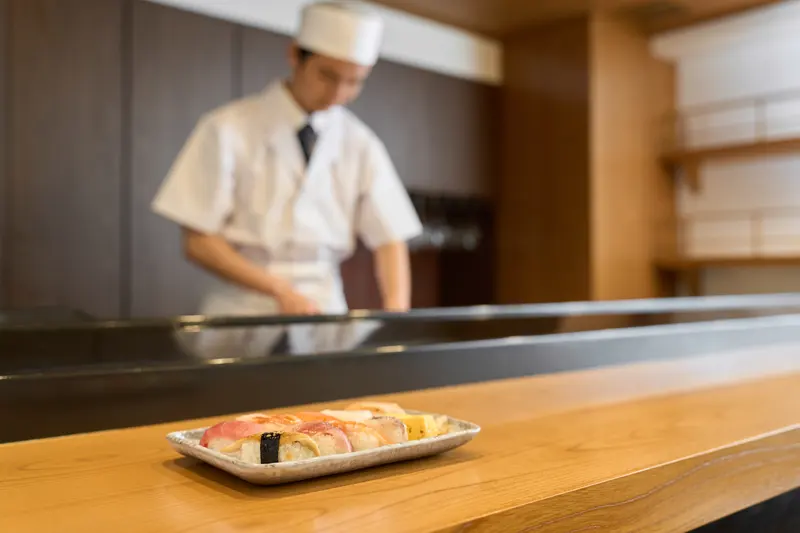Sushikock i vitt bakom disken med ett fat färdiga bitar